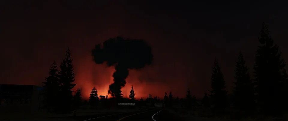 A towering dark cloud rises above a fiery orange horizon beyond a forest road at night.