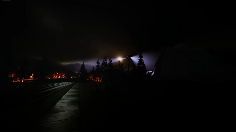 Fires burn beside a dark, wet road as a tripod searchlight glares through the pines.